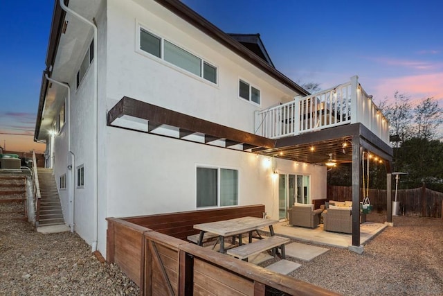 back house at dusk with a balcony, an outdoor living space, a patio, and central air condition unit