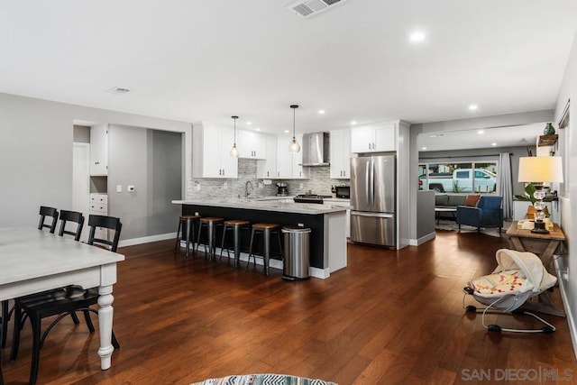 kitchen featuring pendant lighting, wall chimney range hood, stainless steel appliances, light stone countertops, and white cabinets