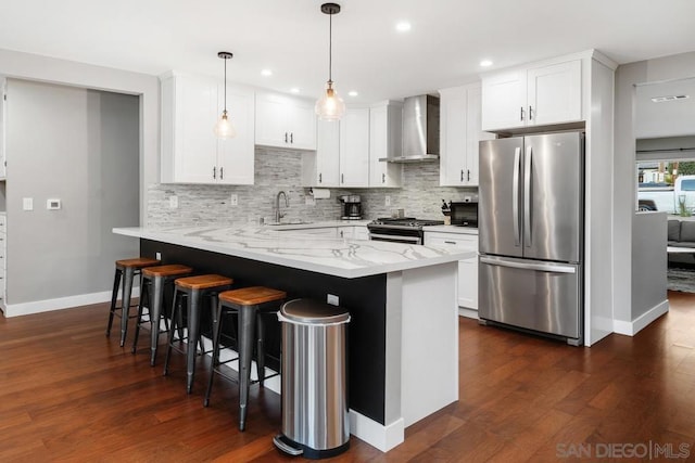 kitchen featuring white cabinetry, decorative light fixtures, wall chimney exhaust hood, and appliances with stainless steel finishes