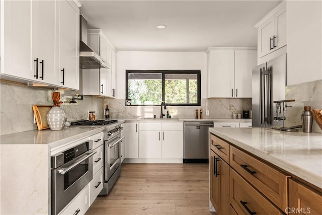 kitchen featuring appliances with stainless steel finishes, wall chimney exhaust hood, white cabinetry, and sink