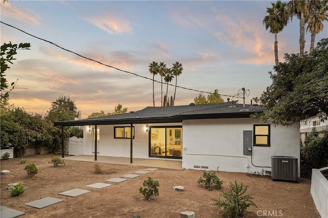 back house at dusk featuring central AC unit and a patio area