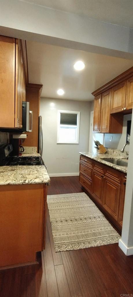 kitchen with light stone countertops, dark wood-type flooring, sink, black gas stove, and stainless steel fridge