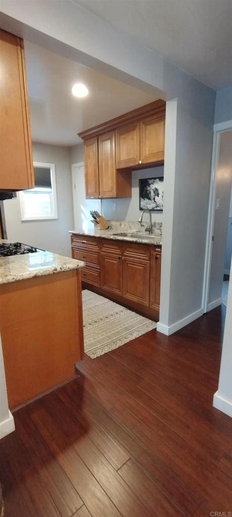 kitchen with light stone countertops, dark wood-type flooring, gas cooktop, and sink