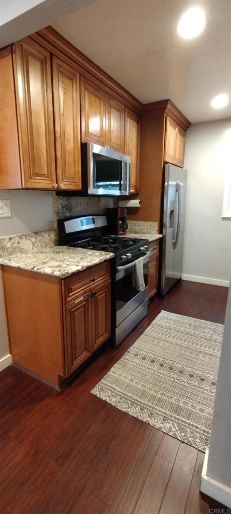 kitchen with light stone counters, appliances with stainless steel finishes, and dark hardwood / wood-style flooring