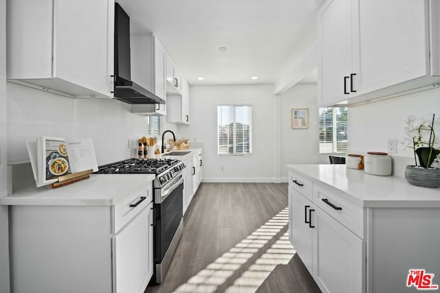 kitchen featuring wall chimney range hood, stainless steel gas range oven, sink, white cabinetry, and dark hardwood / wood-style flooring