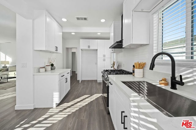 kitchen featuring white cabinetry, stainless steel range with gas cooktop, dark hardwood / wood-style flooring, wall chimney range hood, and sink