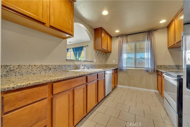 kitchen with a wealth of natural light, stainless steel appliances, light stone counters, and sink