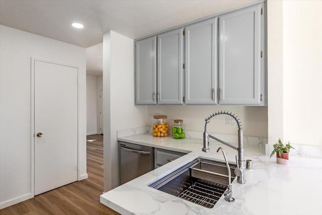 kitchen with gray cabinets, hardwood / wood-style floors, stainless steel dishwasher, sink, and light stone countertops