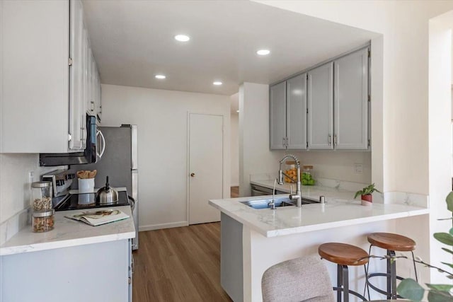 kitchen featuring hardwood / wood-style floors, a kitchen bar, kitchen peninsula, and sink