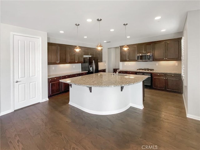 kitchen featuring a breakfast bar, dark hardwood / wood-style floors, hanging light fixtures, a kitchen island with sink, and black appliances