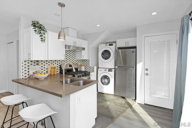 kitchen with stacked washer and dryer, a breakfast bar, stainless steel appliances, white cabinets, and kitchen peninsula