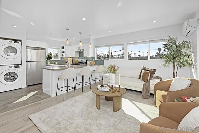 living room with stacked washer / dryer, a wall unit AC, and light hardwood / wood-style floors