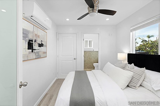 bedroom featuring ceiling fan, an AC wall unit, connected bathroom, and light hardwood / wood-style floors