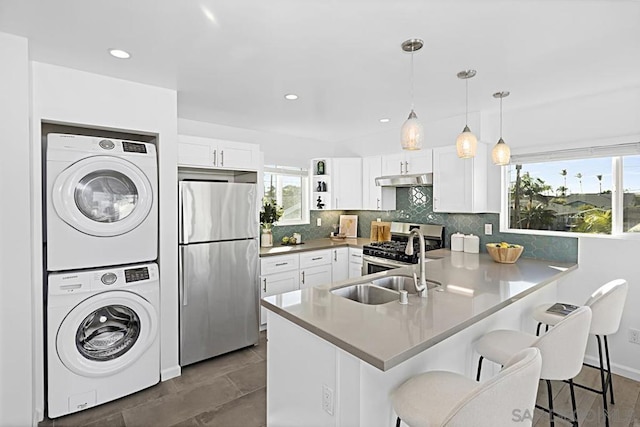 kitchen featuring decorative light fixtures, a breakfast bar area, white cabinets, stacked washer and clothes dryer, and stainless steel appliances