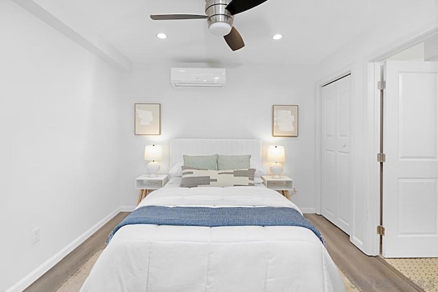 bedroom featuring hardwood / wood-style flooring, a wall mounted AC, ceiling fan, and a closet