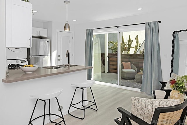 kitchen with a breakfast bar, stainless steel fridge, white cabinets, hanging light fixtures, and kitchen peninsula