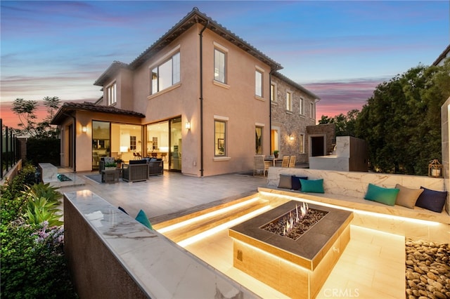 back house at dusk with a patio and an outdoor living space with a fireplace