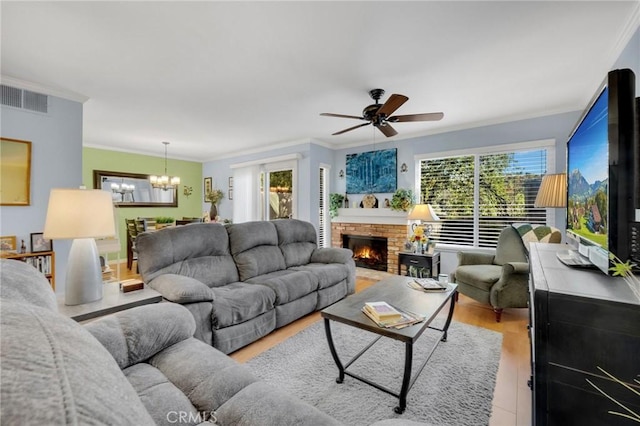 living room with ceiling fan with notable chandelier, light hardwood / wood-style flooring, crown molding, and a fireplace