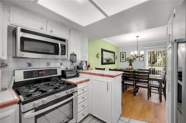 kitchen with tile countertops, pendant lighting, an inviting chandelier, white cabinetry, and stainless steel appliances