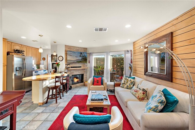 living room featuring a stone fireplace and wood walls