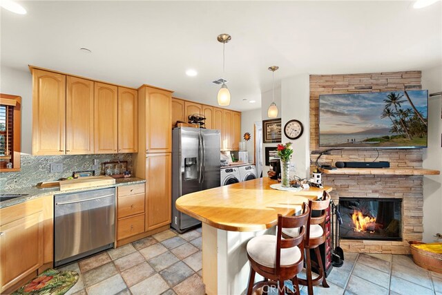 kitchen featuring pendant lighting, backsplash, stainless steel appliances, washing machine and dryer, and a stone fireplace