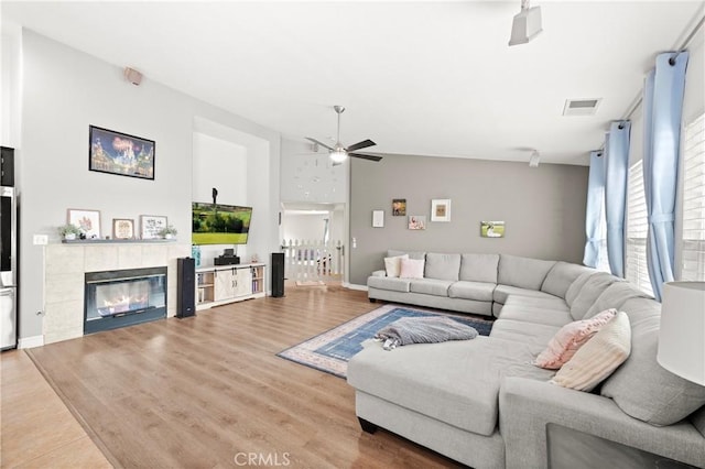 living room with vaulted ceiling, ceiling fan, wood-type flooring, and a tile fireplace