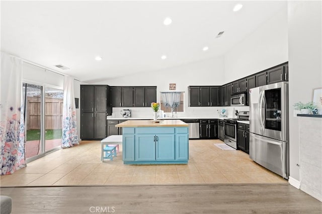 kitchen featuring appliances with stainless steel finishes, lofted ceiling, a kitchen island, sink, and light hardwood / wood-style flooring