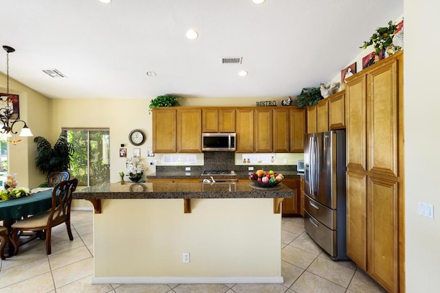 kitchen featuring appliances with stainless steel finishes, tasteful backsplash, hanging light fixtures, a kitchen island with sink, and a breakfast bar area