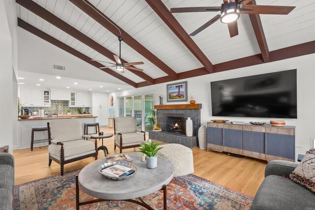 living room with light wood-type flooring, high vaulted ceiling, a tiled fireplace, and beamed ceiling