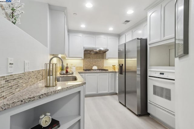 kitchen with white cabinets, stainless steel appliances, sink, backsplash, and light stone counters