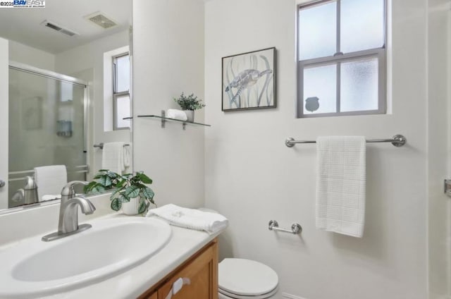 bathroom with toilet, a healthy amount of sunlight, a shower with door, and vanity