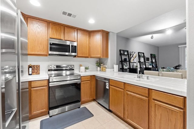 kitchen with rail lighting, sink, light tile patterned floors, appliances with stainless steel finishes, and kitchen peninsula