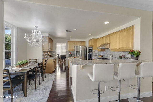 kitchen featuring backsplash, kitchen peninsula, a kitchen bar, appliances with stainless steel finishes, and dark hardwood / wood-style flooring