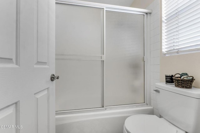 bathroom featuring toilet and combined bath / shower with glass door