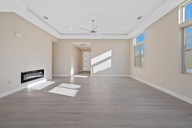 unfurnished living room with ceiling fan, a tray ceiling, and light hardwood / wood-style floors