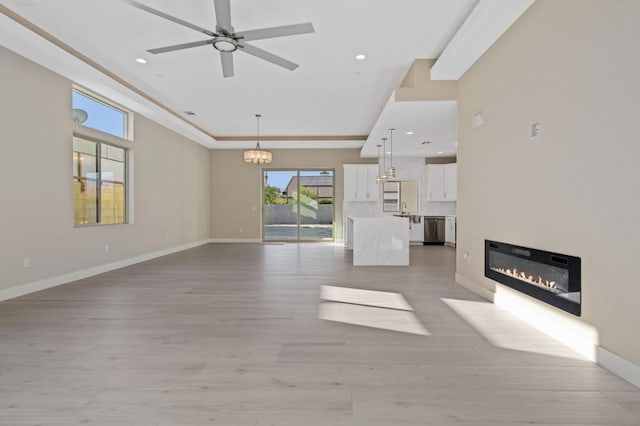 unfurnished living room with ceiling fan with notable chandelier and light hardwood / wood-style flooring