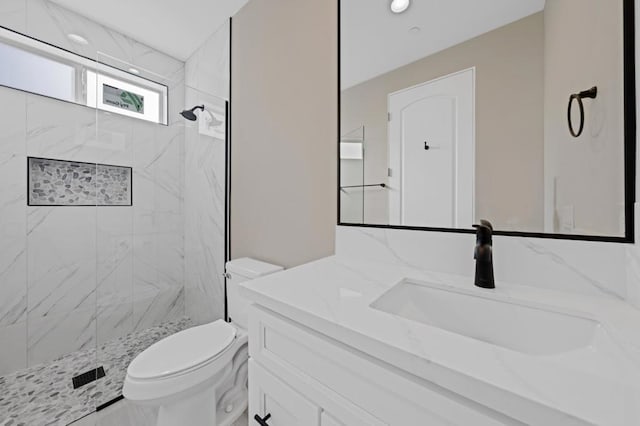 bathroom featuring toilet, tiled shower, and vanity