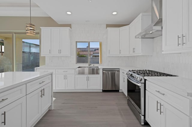 kitchen with white cabinetry, wall chimney range hood, appliances with stainless steel finishes, and pendant lighting