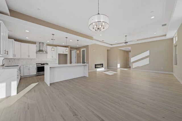 kitchen featuring white cabinetry, stainless steel range, decorative light fixtures, a kitchen island, and wall chimney exhaust hood