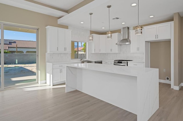 kitchen with gas range, a center island, white cabinets, and wall chimney range hood