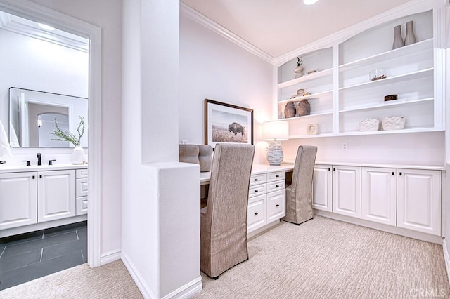 office area with crown molding, built in desk, light colored carpet, a sink, and baseboards