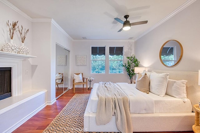 bedroom with baseboards, a fireplace with raised hearth, a ceiling fan, wood finished floors, and crown molding