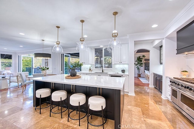 kitchen featuring range with two ovens, pendant lighting, a large island, white cabinetry, and a sink