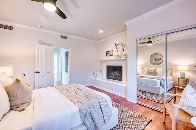 bedroom with visible vents, a fireplace with raised hearth, wood finished floors, and ornamental molding