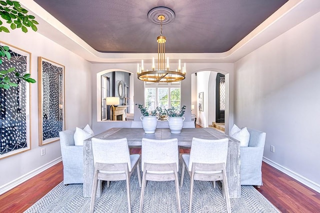 dining space featuring baseboards, a tray ceiling, wood finished floors, and an inviting chandelier