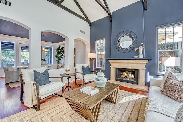 living area featuring high vaulted ceiling, a fireplace, visible vents, and wood finished floors