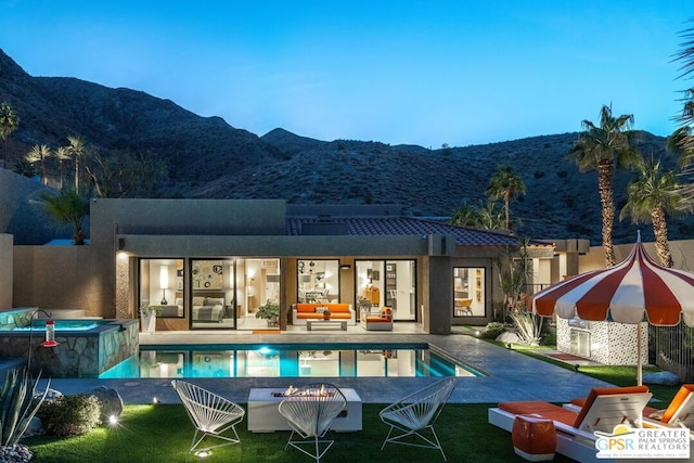 back house at dusk with a mountain view, a patio area, a pool with hot tub, and an outdoor living space