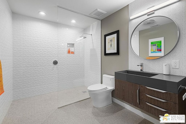 bathroom with a tile shower, toilet, and vanity