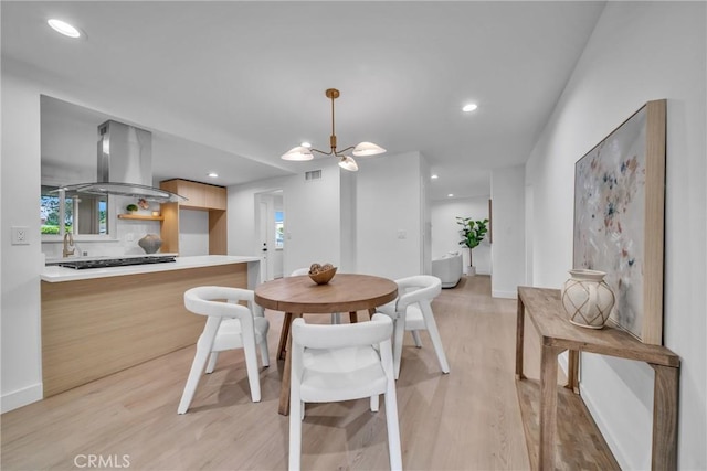 dining space with light wood-type flooring, a notable chandelier, and sink