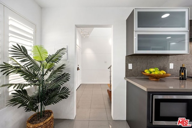 kitchen featuring decorative backsplash, stainless steel microwave, and light tile patterned flooring